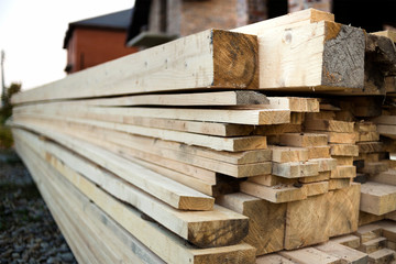 Poster - Stack of natural brown uneven rough wooden boards on building site. Industrial timber for carpentry, building, repairing and furniture, lumber material for roofing construction.