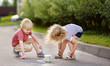 Happy little boy and girl drawing with colored chalk on asphalt