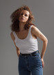 © Sergey Chumakov - young curly woman in jeans and white t-shirt on studio gray background