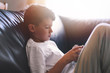Little lonely boy playing on smartphone on sofa