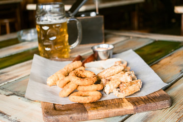 Glasses of light beer on pub background. Pint glass of golden beer with snacks and grill food on wooden table in pub, bar