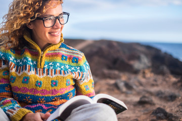 Woman sit down on the rocks in outdoor beautiful place with ocean in background reading a paper book and enjoying the freedom and the relax situation. Smile and happy people concept