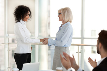 Sticker - Mature team leader female ceo congratulating happy successful african american office worker with promotion, smiling aged boss shaking hand of young mixed race employee excited by reward recognition