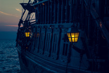 Yellow Illumination From Soft Focus Vintage Lamp In Over Board Of Wooden Old Pirate Ship On Sea Surface Landscape With Horizon Line In Evening Dark Twilight Time  