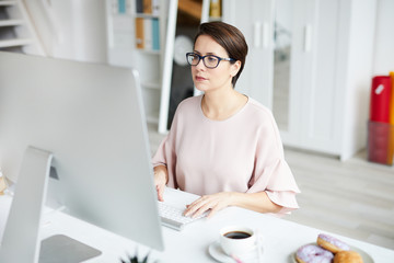 Young elegant businesswoman looking at computer screen while networking by desk in office