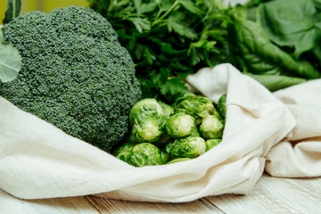 Wall Mural - Broccoli, brussels sprouts, spinach and parsley in the canvas reusable bag on the wooden table. Less plastic grocery concept. Closeup food photo of local market products 