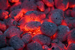 Coals smolder and glow. Residual flame from smoldering coals in cinder, closeup view. Flicker of burning coals at night.