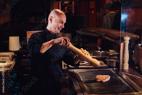 Fotografía Master chef cooking delicious beef steak on a kitchen in a restaurant, pepper the meat with a pepper mill