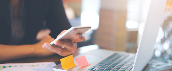 Business women hand are uses a smartphone and use a laptop computer in office.