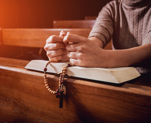 Wall Mural - Christian woman praying in church. Hands crossed and Holy Bible on wooden desk.