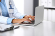 © rogerphoto - Unknown doctor woman typing on laptop computer while sitting at the desk in hospital office. close-up of hands. Physician at work. Medicine and health care concept
