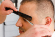 Scissors cutting eyebrow of man at barbershop. Brow grooming close up.