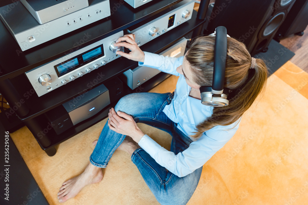 Woman with headphones listening to music via the Hi-Fi stereo in her home - obrazy, fototapety, plakaty 