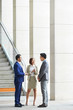 © DragonImages - Multiethnic group of business people standing and talking to each other before meeting at office corridor