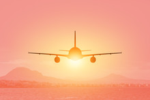 Silhouette Of Airplane Flying Over The Sea And Beach At Sunset. Travel Concept.