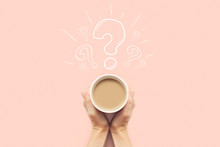 A Hand Is Holding A Cup With Hot Coffee On A Pink Background. Question Mark. Breakfast Concept With Coffee Or Tea. Good Morning, Night, Insomnia. Flat Lay, Top View