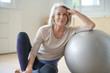 Leinwandbild Motiv  Smiling elderly woman resting on a swiss ball at home