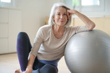 Fototapeta  -  Smiling elderly woman resting on a swiss ball at home