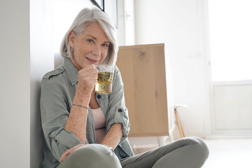 Wall Mural -  Attractive senior woman sitting on the floor at home with tea