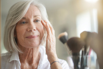 Attractive senior woman looking at herself in mirror