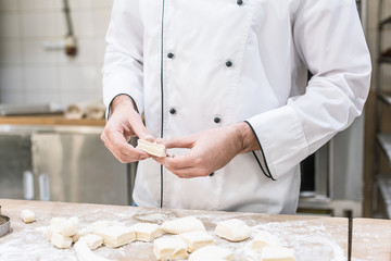 Wall Mural - Cropped view of baker in chefs uniform cooking dough on wooden table