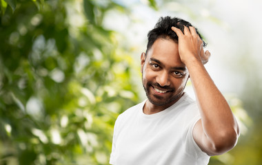 grooming and people concept - smiling young indian man touching his hair over green natural background