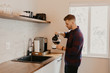 © MeganMahoneyPhotos - Young Attractive Minimalist Hipster Man in Modern Designed Kitchen Brews, Pours, and Drinks Morning Coffee out of a Cup