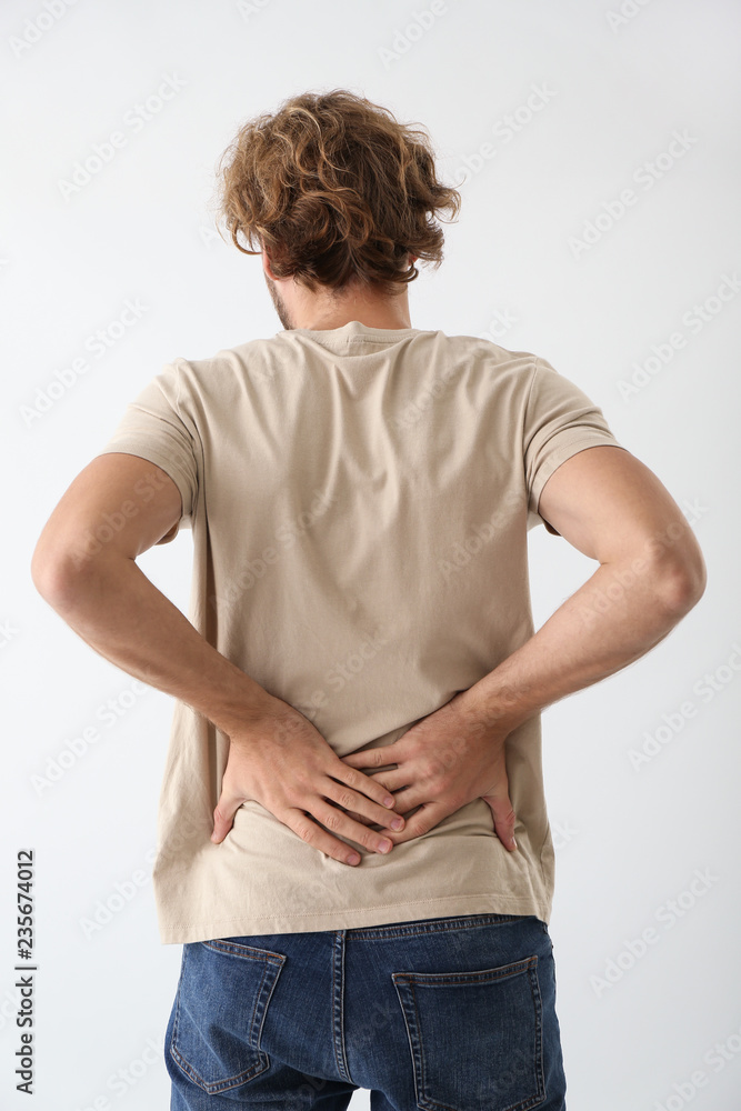 Young man suffering from back pain on light background