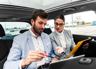 Wall Mural - Young business people working together while traveling by a car. They are using laptop and preparing for meeting.	