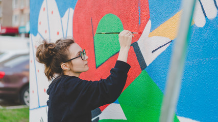 Girl paints mural on the wall with a brush, color wall