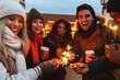 © Drobot Dean - Young friends talking with each other drinking coffee outdoors winter concept holding bengal lights.