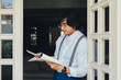 © LUMINA IMAGES - Serious elegant middle-aged Asian man standing by the open window and reading from notebook.