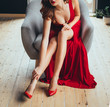 © kharchenkoirina - sexy red-haired young woman playfully touches her fingers over her bare leg, showing the neckline. in a long scarlet expensive delightful long luxurious dress and red high-heeled shoes