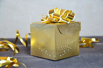 gold box with a gift for Christmas with gold ribbon and bow for a birthday or holiday on a brown wooden background