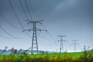 High voltage lines and power pylons in a green agricultural landscape at rainy day with.