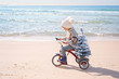 Santa claus kid in Christmas sweater. Happy child on the bicycle or tricycle near water. Xmas party celebration, childhood. Winter holiday vacation. New year small boy at sea beach.
