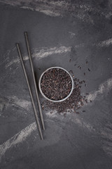 Wall Mural - Top view of uncooked black rice in gray bowl with wooden chinese chopsticks