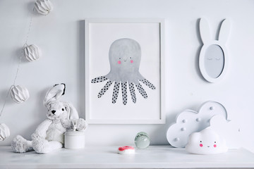 Stylish scandinavian nursery shelf with mock up photo frame, white rabbit and toys. Modern interior with white walls and wooden accessories.