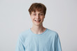 Teenager with short hair and braces on teeth looks camera, wears blue t-shirt, feels happy glad, smiling isolated over white background