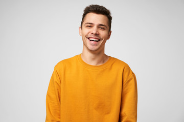 Wall Mural - Cheerful positive male youngster, dressed casually, glad to spend time with friends, joking laughing, has a good time. Positive emotions and feelings, isolated over white background