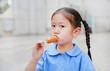 © zilvergolf - Adorable little Asian child girl in school uniform enjoy eating sausage.