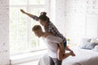 Excited happy young woman piggyback man in bedroom, loving couple having fun together at home, laughing spouses in new own apartment, looking forward to good future, husband carrying wife on his back