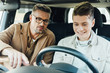 © LIGHTFIELD STUDIOS - handsome father pointing on something while teaching smiling teen son driving car