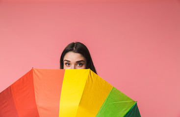 Sticker - Emotional young woman posing isolated over pink background holding rainbow umbrella.