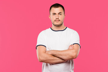 confident handsome young man posing with crossed arms isolated on pink