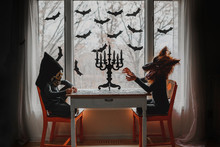 Two Children In Halloween Costumes Sitting By A Window Doing A Puzzle, United States