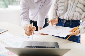 Wall Mural - faceless shot of man and woman with papers discussing new project using laptop at desk