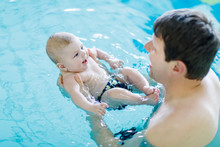 Happy Middle-aged Father Swimming With Cute Adorable Baby In Swimming Pool. Smiling Dad And Little Child, Newborn Girl Having Fun Together. Active Family Spending Leisure And Time In Spa Hotel