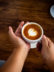 Wall Mural - Girl holding cup of cafe latte on wooden table