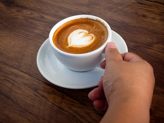 Wall Mural - Girl holding cup of cafe latte on wooden table